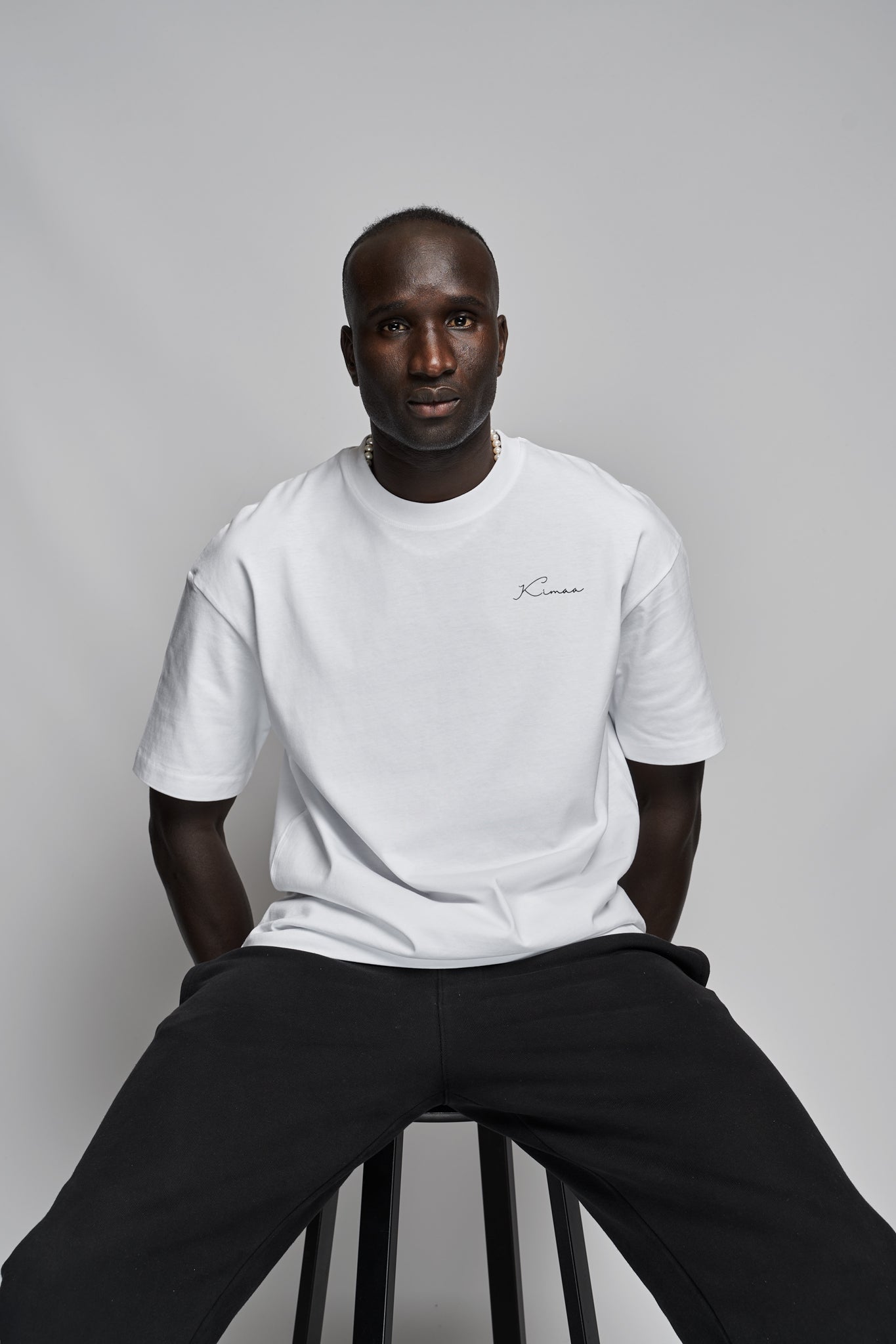 Model seated wearing Senumaa white tee by Kimaa, showcasing casual fit and soft structure.