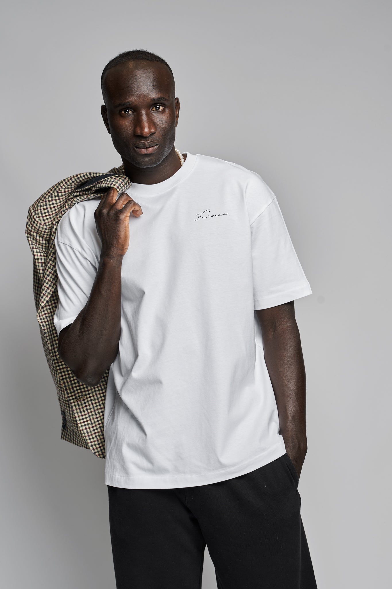 Model styling white Senumaa T-shirt with a patterned coat, Afro-Nordic fashion by Kimaa.