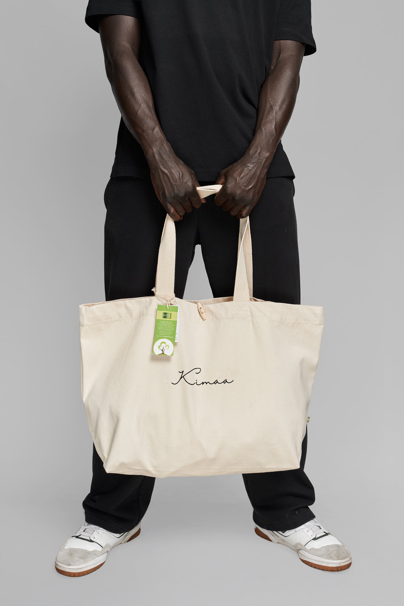 Beige Kimaa tote bag held straight down in front of body, emphasizing natural tone and structured design.