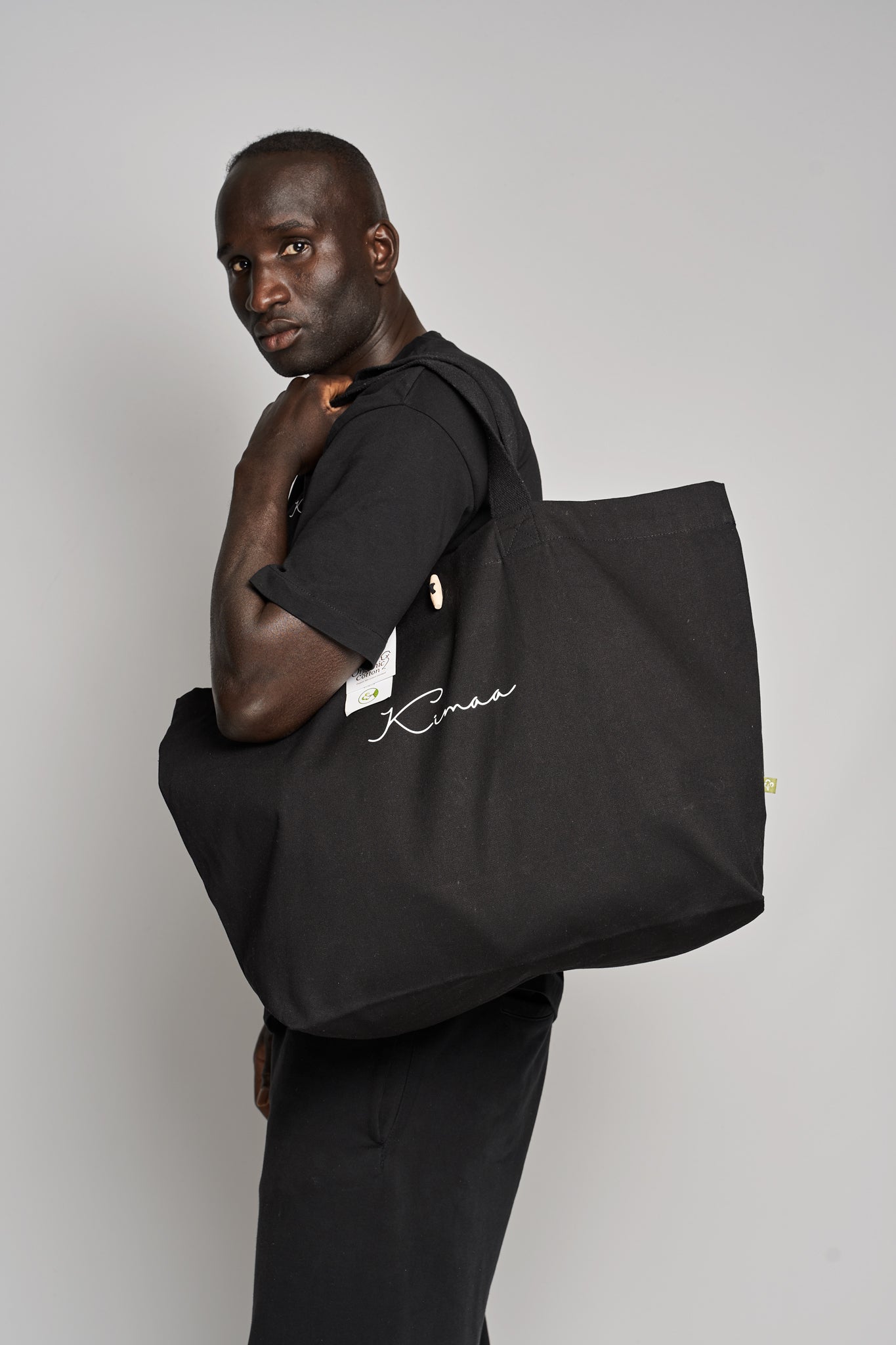 Black Maabo organic cotton tote bag worn on shoulder with soft handles and wooden toggle closure
