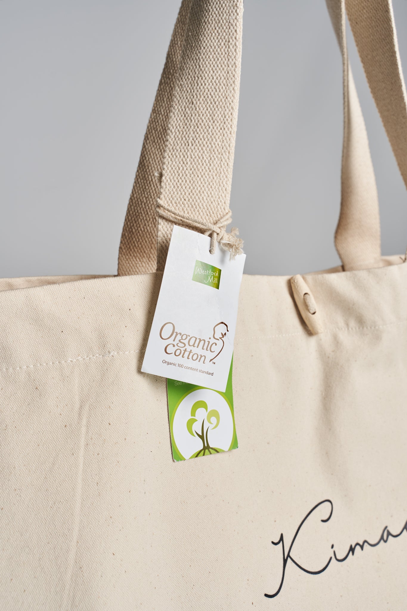 Closeup of organic cotton label hanging from handle of Kimaa’s Taamoo tote bag.