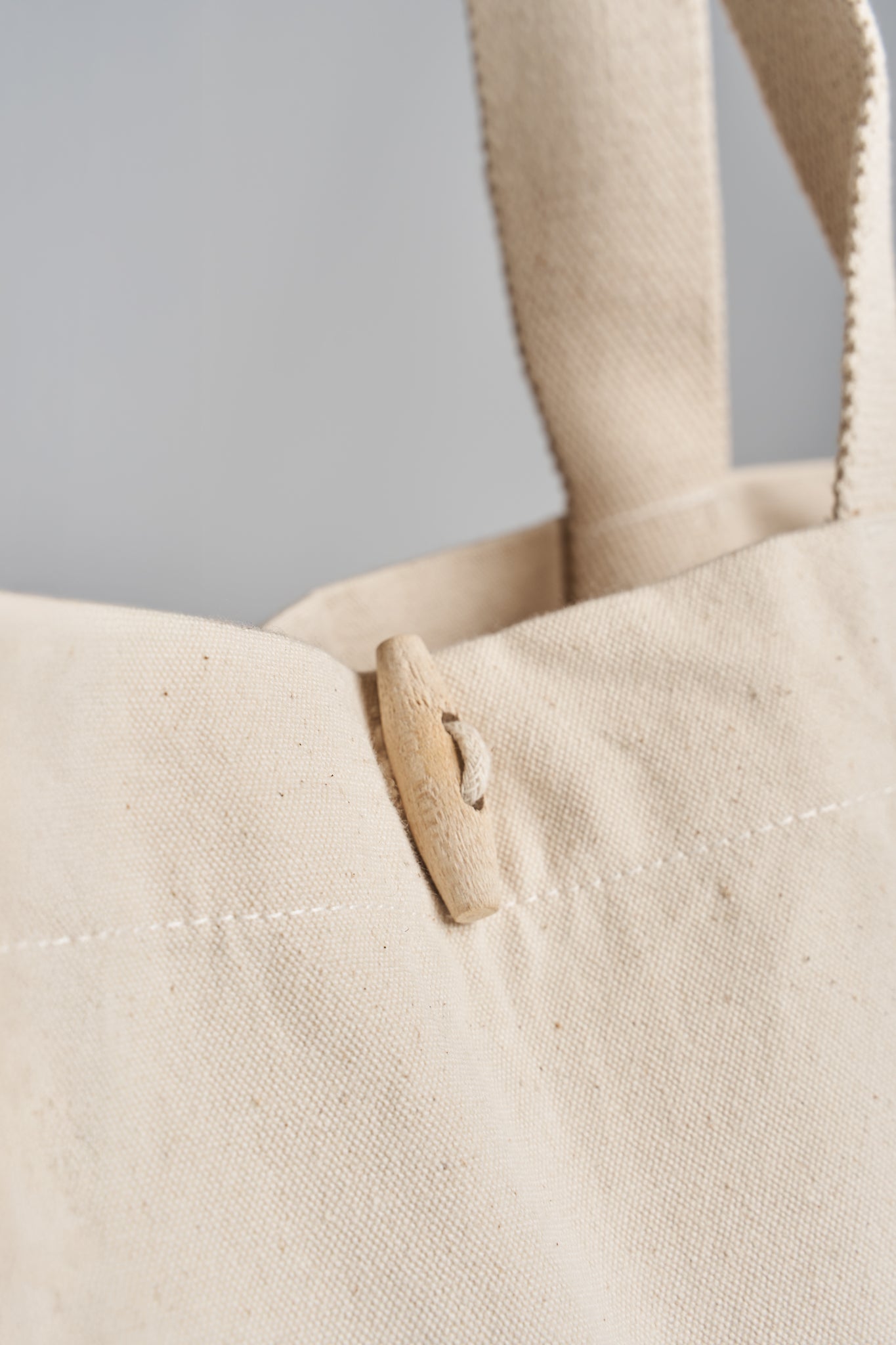Detailed closeup of wooden toggle closure on the beige Kimaa Taamoo tote bag.